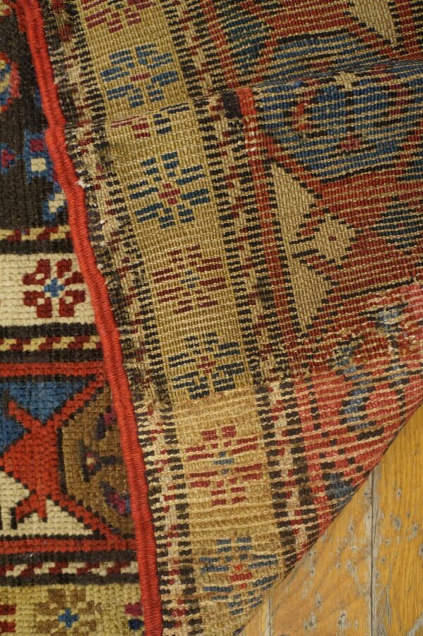 Knotted rug edge and flat woven backing in red, blue, and gold resting on distressed wood floor.