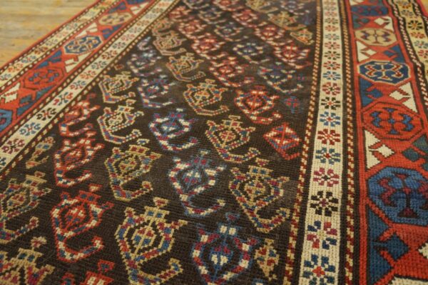 Low-pile rug with dark field, geometric red and blue motifs, and intricate borders rests on wood floor.