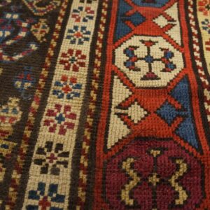 Close-up of a geometric rug with red, blue, cream, and burgundy motifs on a dark brown field.