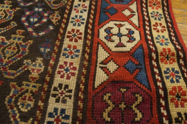Close-up of a geometric rug with red, blue, cream, and burgundy motifs on a dark brown field.