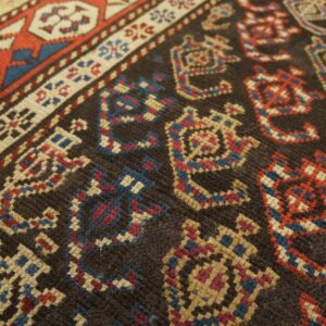 Geometric motifs in red, blue, and beige stand out against the dark brown, low-pile rug field.