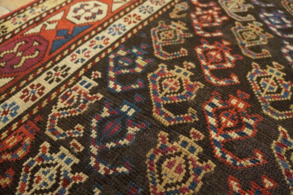 Geometric motifs in red, blue, and beige stand out against the dark brown, low-pile rug field.