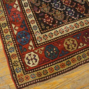 Geometric rug detail showing borders in red, tan, and blue surrounding a dark patterned field on wood flooring.