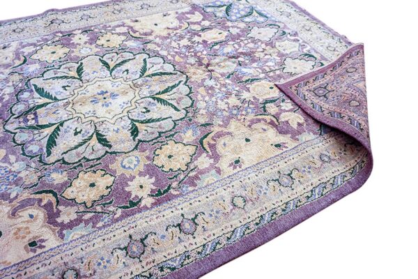 Low-pile traditional rug featuring purple, beige, and green floral patterns, with a corner folded over against white.