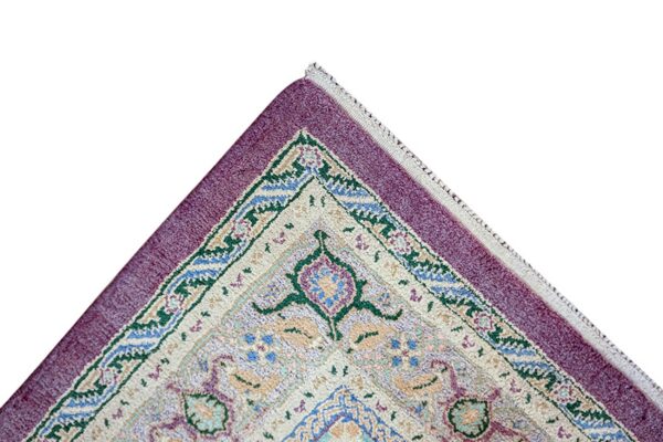 Corner detail of a patterned rug featuring teal, blue, and cream motifs next to a solid purple border.