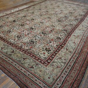 Muted low-pile rug featuring complex red, black, and pale tan designs rests on wide distressed wood flooring.