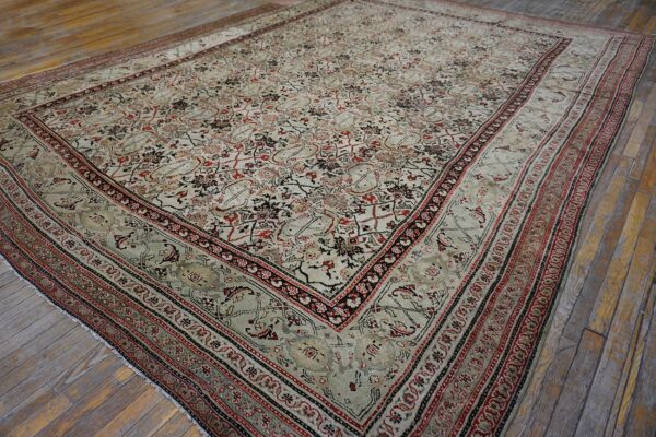 Muted low-pile rug featuring complex red, black, and pale tan designs rests on wide distressed wood flooring.