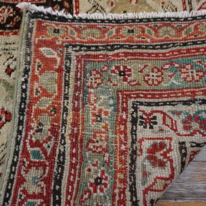Close-up of two geometric patterned rugs, featuring red, teal, cream, and black colors, resting on distressed wood.
