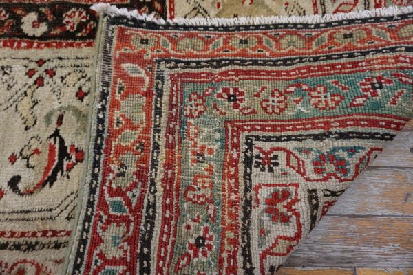 Close-up of two geometric patterned rugs, featuring red, teal, cream, and black colors, resting on distressed wood.