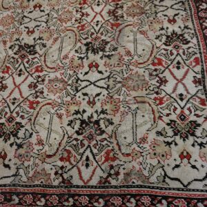 Low-pile rug with complex black and red traditional patterns over a distressed cream background and border.