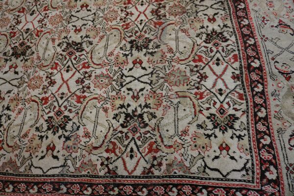 Low-pile rug with complex black and red traditional patterns over a distressed cream background and border.