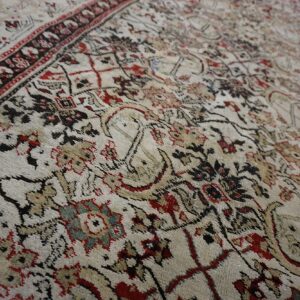Low-pile rug detailed with complex traditional patterns in cream, black, red, tan, and muted blue.