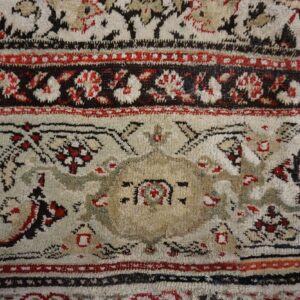 Close-up of a rug featuring an elaborate design in cream, dark red, black, and beige colors.