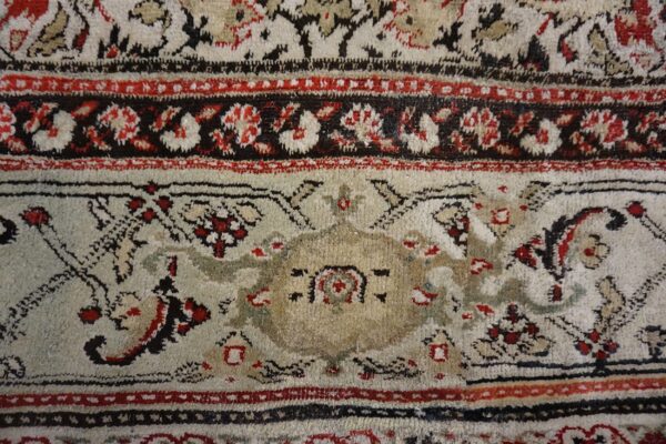 Close-up of a rug featuring an elaborate design in cream, dark red, black, and beige colors.