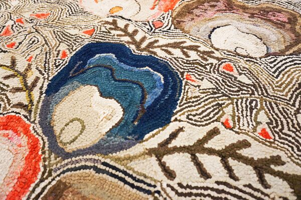 Textured rug detail with large blue, brown, and red organic shapes outlined by wavy cream and brown lines.