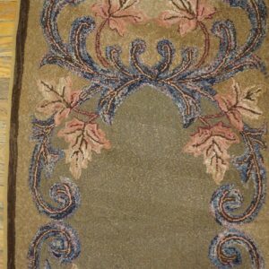 Mottled khaki textured rug displays pink and blue scrolling botanical patterns on wood flooring.