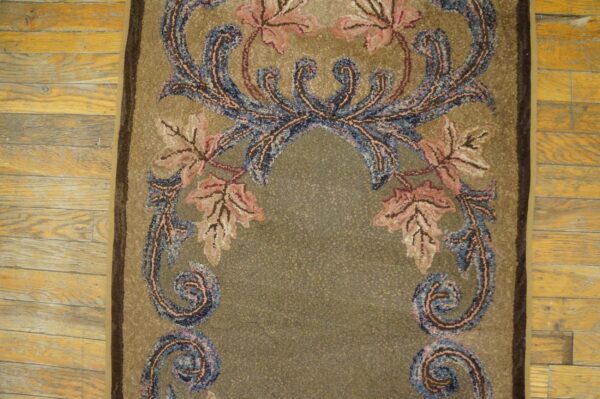 Mottled khaki textured rug displays pink and blue scrolling botanical patterns on wood flooring.