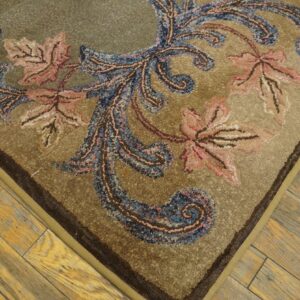 Highly textured tan rug featuring blue and salmon baroque motifs lies on worn wood plank flooring.