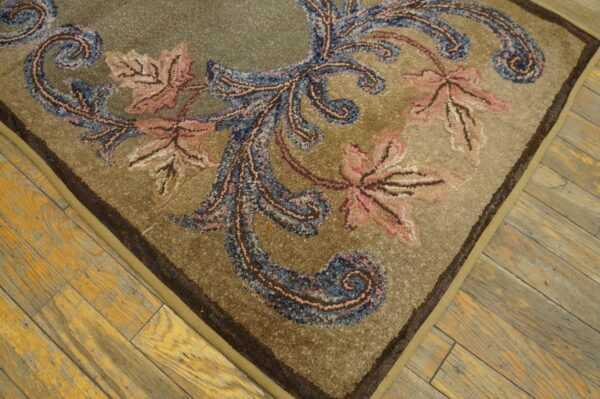 Highly textured tan rug featuring blue and salmon baroque motifs lies on worn wood plank flooring.