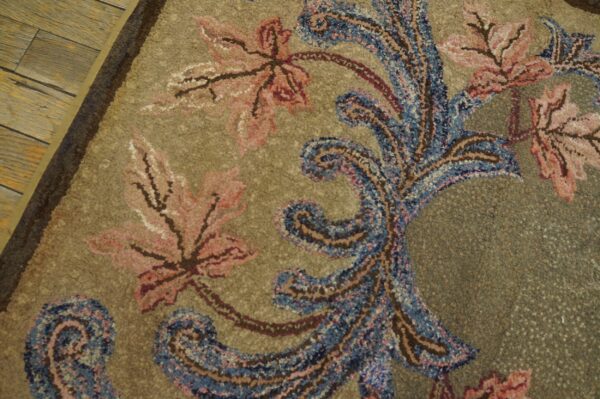 Ornate high-pile rug with pink leaves and blue paisley scrolls on a speckled khaki background next to wood flooring.