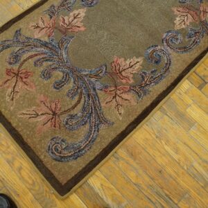 Tan hooked rug featuring pink maple leaves and blue scrolling vines rests on aged wood planks.