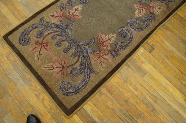 Tan hooked rug featuring pink maple leaves and blue scrolling vines rests on aged wood planks.