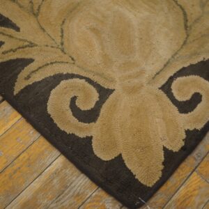 Low-pile, tan and dark brown hooked rug displaying a scrolling floral pattern rests on distressed wood planks.