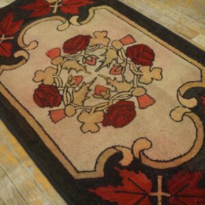 A hooked texture rug featuring red roses and tan leaves on an ivory center, surrounded by a dark brown border.