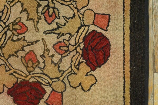 Close-up detail of a textured beige rug featuring red and tan stylized flowers with a multi-striped border.