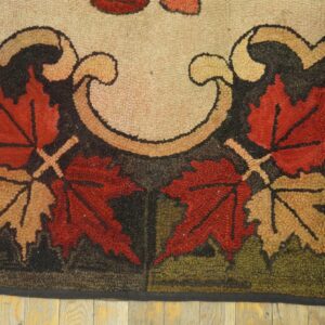 Hooked rug with red and tan maple leaf design on a dark ground rests on light wood floors.