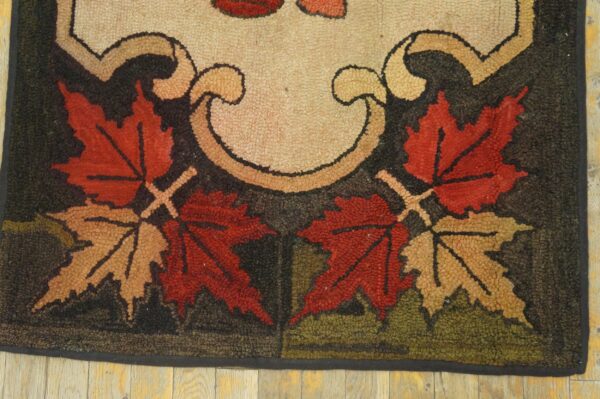 Hooked rug with red and tan maple leaf design on a dark ground rests on light wood floors.