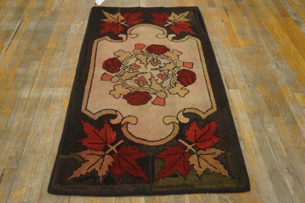 Dark floral hooked rug with red and tan leaves on a cream center, set on worn wooden floorboards.