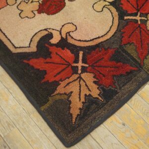 Chunky-pile rug corner with autumn leaf patterns in red and tan rests on rustic wood flooring.