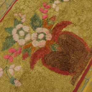 Golden looped rug with pink florals and a brown vase resting on rustic yellow wood planks.