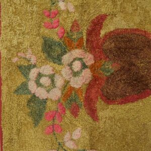 Close-up of a gold shag rug featuring pink, green, and brown floral patterns, bordering worn wood plank flooring.
