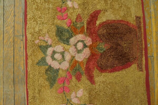 Close-up of a gold shag rug featuring pink, green, and brown floral patterns, bordering worn wood plank flooring.