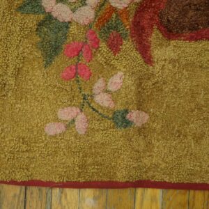 Hooked rug with mustard yellow texture and pink floral design sits on distressed wood floorboards.