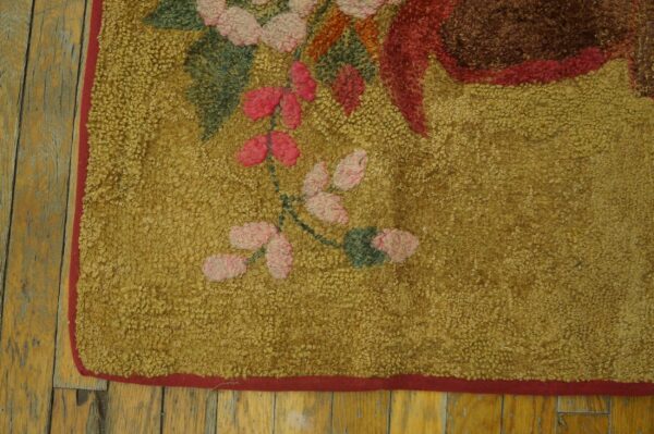 Hooked rug with mustard yellow texture and pink floral design sits on distressed wood floorboards.