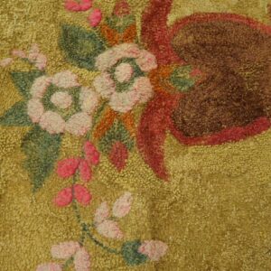 Highly textured gold rug with floral elements in pink, green, and deep brown, visible on wood planks.