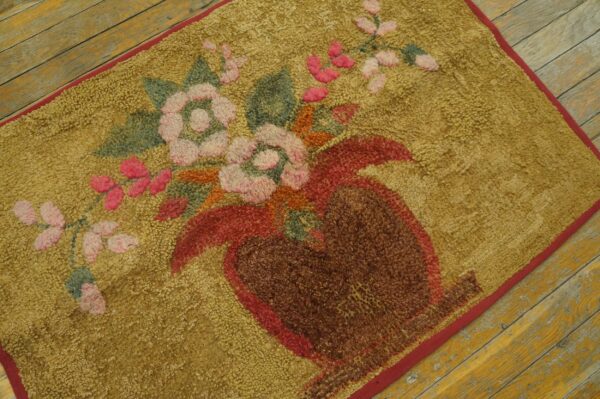 A shaggy golden yellow rug featuring a stylized pink and red floral vase design rests on worn wood flooring.
