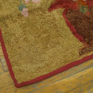Close up of a looped mustard rug with a brown and red floral pattern on distressed yellow wood flooring.