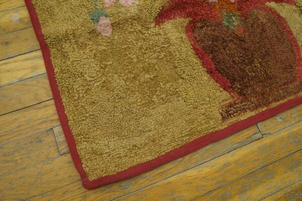 Close up of a looped mustard rug with a brown and red floral pattern on distressed yellow wood flooring.