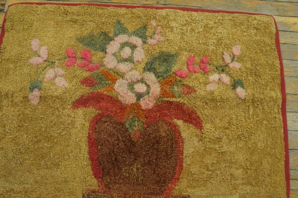 Hooked gold rug displaying a central floral bouquet in pink, red, and green on rustic wood flooring.
