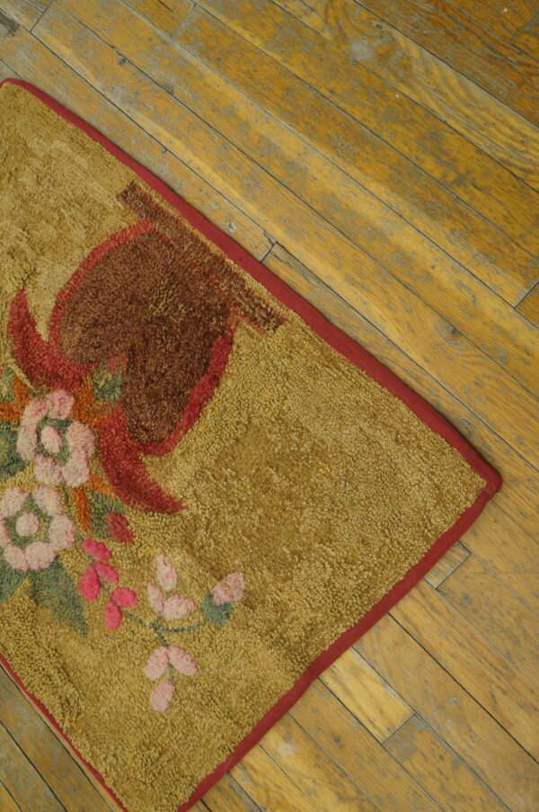 Textured loop pile rug in gold features a red, pink, and brown floral pattern against distressed wood flooring.
