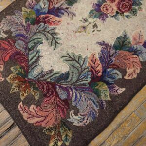 Multicolored floral hooked rug featuring a cream center and dark border rests on distressed wooden planks.