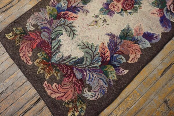 Multicolored floral hooked rug featuring a cream center and dark border rests on distressed wooden planks.