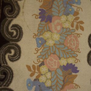 Close-up of a textured rug showing a dense band of pink, blue, and yellow flowers with a dark scroll border.