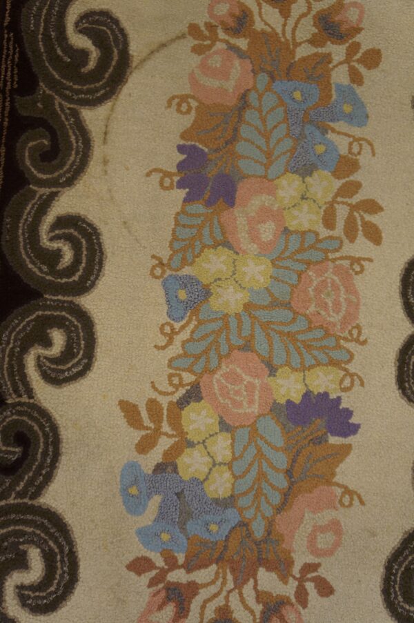 Close-up of a textured rug showing a dense band of pink, blue, and yellow flowers with a dark scroll border.