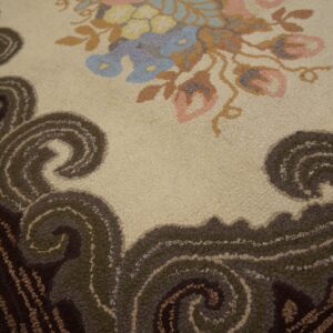Hooked rug featuring pink and blue flowers on cream, bordered by dark brown and olive green scrolls.