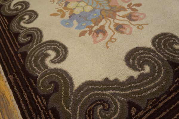 Hooked rug featuring pink and blue flowers on cream, bordered by dark brown and olive green scrolls.